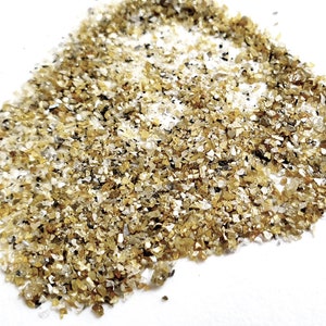 May include: A pile of small, golden, and clear quartz crystals on a white surface.