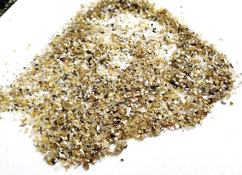 May include: A pile of small, golden, and clear quartz crystals on a white surface.