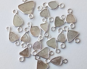 May include: A group of 20 silver-toned metal charms with a rough, clear, and white gemstone in the center of each charm. Each charm has two loops for attaching to jewelry.