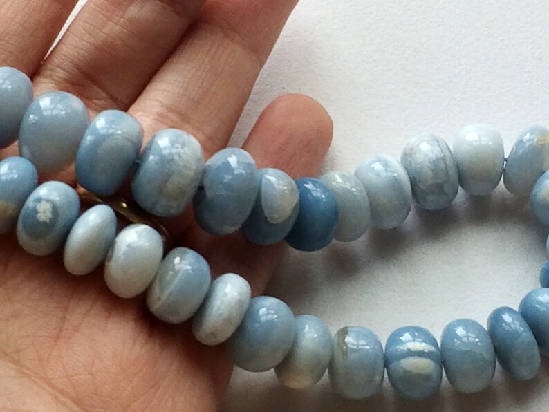 May include: A strand of light blue gemstone beads with a white marbled pattern. The beads are round and smooth, and they are strung on a clear thread.
