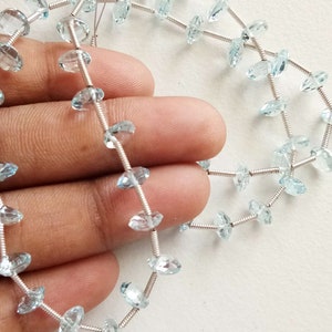 May include: A strand of light blue aquamarine gemstone beads strung on silver wire. The beads are faceted and have a teardrop shape.