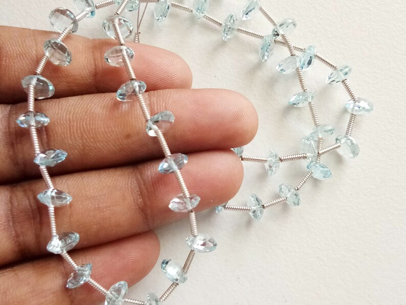 May include: A strand of light blue aquamarine gemstone beads strung on silver wire. The beads are faceted and have a teardrop shape.
