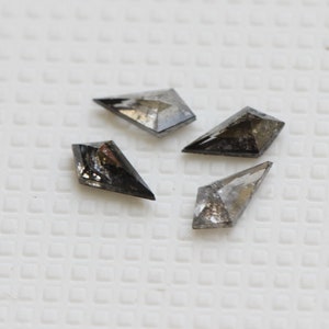 May include: Four black diamond gemstones with a kite shape and a pointed tip. The diamonds are arranged in a loose cluster on a white surface.