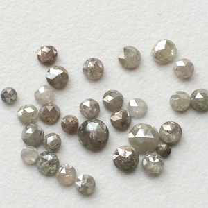 May include: A collection of round, faceted, grey diamonds with a rough, natural finish. The diamonds are scattered on a white surface.