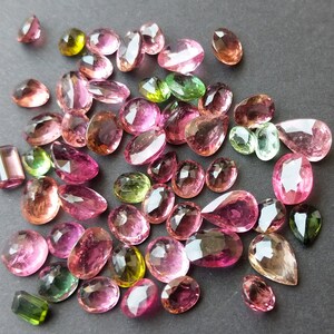 May include: Assortment of faceted gemstones in various shapes and sizes, including oval, pear, and rectangular cuts. The gems display a range of colors, such as pink, green, and brown, with a polished, reflective surface. Ideal for jewelry making.
