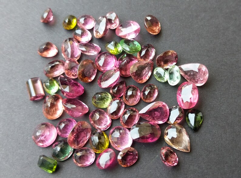 May include: Assortment of faceted gemstones in various shapes and sizes, including oval, pear, and rectangular cuts. The gems display a range of colors, such as pink, green, and brown, with a polished, reflective surface. Ideal for jewelry making.