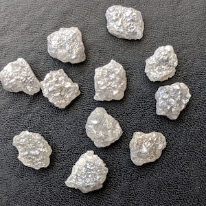 K&ouml;nnte beinhalten: Zehn rohe, wei&szlig;e Diamantkristalle auf schwarzem Hintergrund.