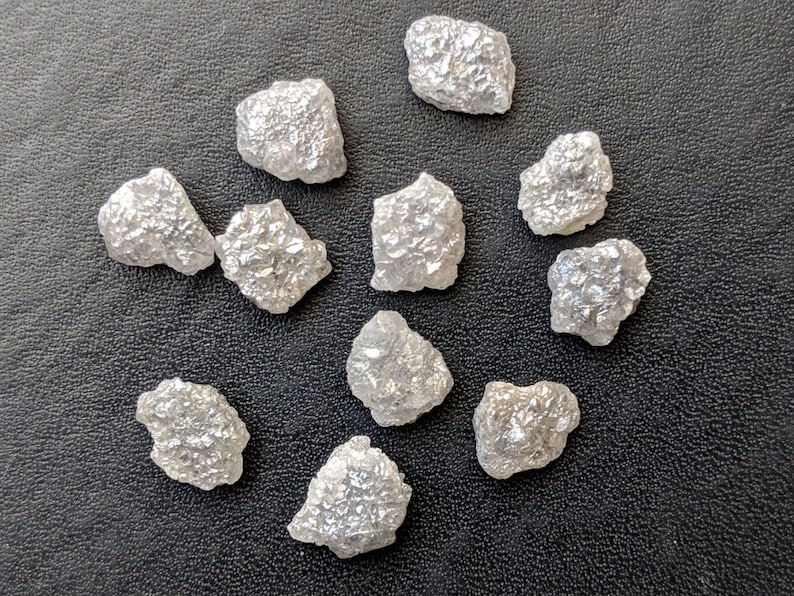 K&ouml;nnte beinhalten: Zehn rohe, wei&szlig;e Diamantkristalle auf schwarzem Hintergrund.
