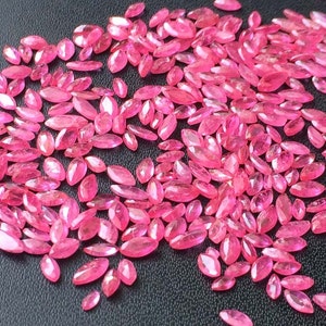 Op de afbeelding: Een grote groep roze marquise-vormige edelstenen. De edelstenen zijn verspreid over een zwart oppervlak.