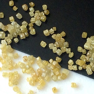 May include: A close-up view of a collection of small, yellow, faceted diamonds. The diamonds are scattered on a black and white surface.