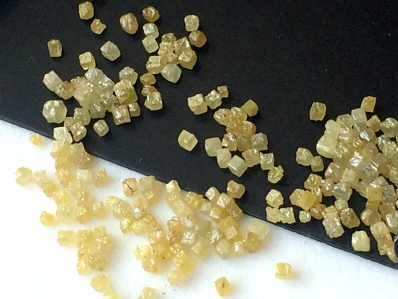 May include: A close-up view of a collection of small, yellow, faceted diamonds. The diamonds are scattered on a black and white surface.