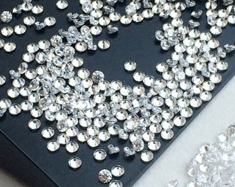 May include: A close-up image of a large quantity of loose, round, clear, faceted gemstones. The gemstones are scattered on a black surface.