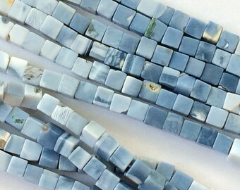 Puede incluir: Una hebra de cuentas de piedra preciosa de forma cuadrada de color azul claro, blanco y gris. Las cuentas tienen un patrón de mármol y miden aproximadamente 8 mm.
