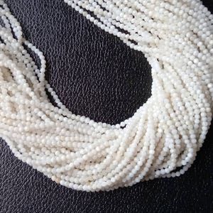 May include: A strand of white moonstone beads, each bead is faceted and has a slightly iridescent sheen.