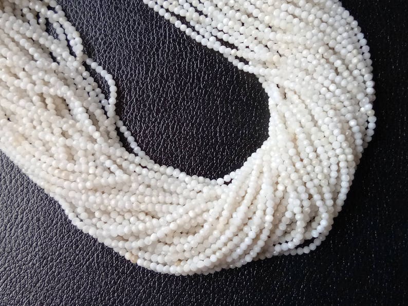 May include: A strand of white moonstone beads, each bead is faceted and has a slightly iridescent sheen.