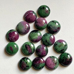 May include: A collection of 15 round, green and pink gemstone cabochons. The cabochons are smooth and polished, with a variety of patterns and colors.