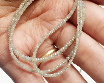 May include: A strand of white diamond beads, strung on a thin wire, is draped over a hand. The beads are small and uniform in size, and they have a subtle sparkle.