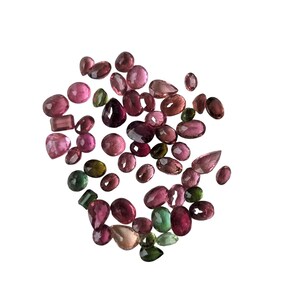 May include: A collection of polished gemstones in various shapes and sizes, including oval, pear, and round cuts. The gems display a range of colors from deep burgundy to light pink and green, set against a white background. Ideal for jewelry making or collecting.