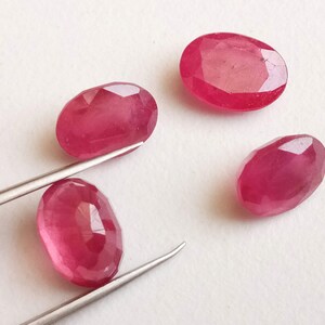 May include: Four oval-shaped, faceted ruby gemstones. The rubies are a deep red color and have a glossy finish.