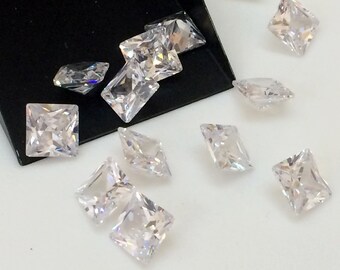 May include: A collection of clear, faceted, square-shaped gemstones. The gemstones are scattered on a white surface.