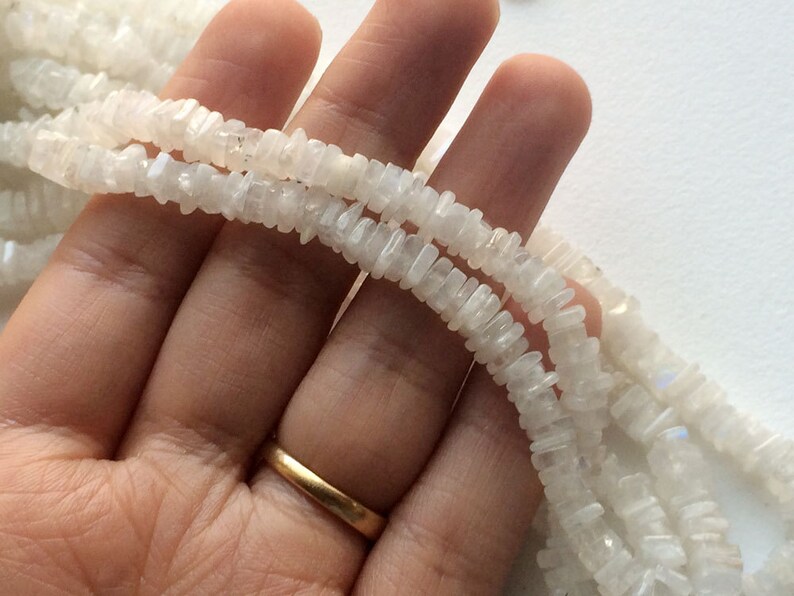 Puede incluir: Una hebra de cuentas de piedra lunar blanca, cada cuenta tiene forma de chip rectangular.