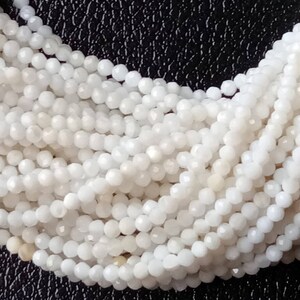 May include: A strand of white gemstone beads, each bead is faceted and has a slightly iridescent sheen. The beads are small and uniform in size.
