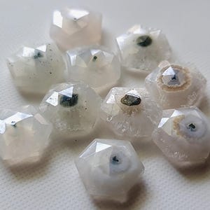 May include: A collection of ten white agate cabochons with green and brown inclusions. The cabochons are faceted and have a rounded shape.