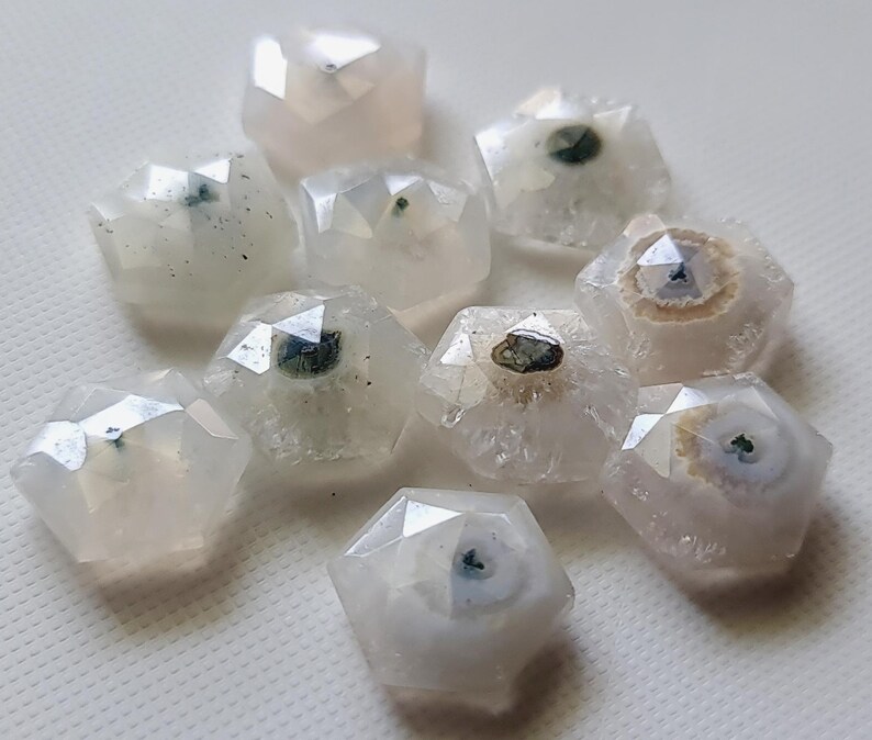 May include: A collection of ten white agate cabochons with green and brown inclusions. The cabochons are faceted and have a rounded shape.