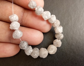 Könnte beinhalten: Eine Strähne aus weißen, rohen Diamantperlen, auf einem Silberdraht aufgereiht. Die Perlen sind rund und haben eine raue, strukturierte Oberfläche.