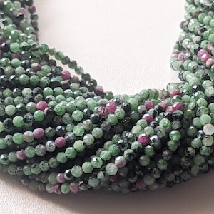 May include: A strand of green and pink faceted gemstone beads. The beads are small and round, and they are strung together on a clear thread.