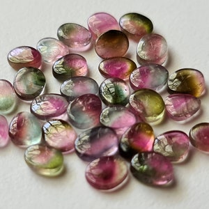 Peut inclure: Une collection de pierres pr&eacute;cieuses ovales multicolores. Les pierres sont un m&eacute;lange de vert, de rose et de noir.