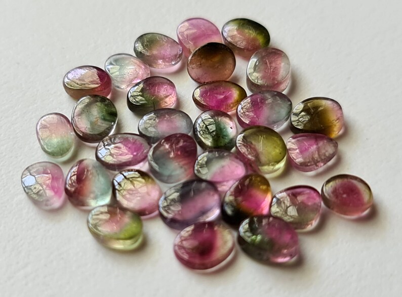 Peut inclure: Une collection de pierres pr&eacute;cieuses ovales multicolores. Les pierres sont un m&eacute;lange de vert, de rose et de noir.