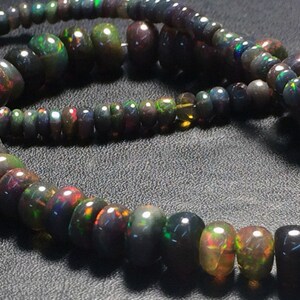 May include: A strand of black opal beads with iridescent rainbow colors. The beads are various sizes and shapes, some round and some more elongated. The beads are strung on a clear thread.