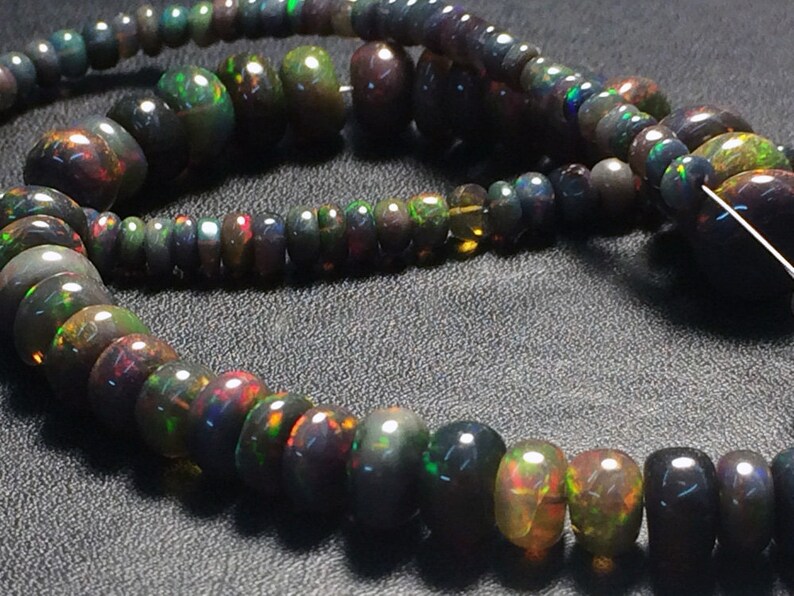 May include: A strand of black opal beads with iridescent rainbow colors. The beads are various sizes and shapes, some round and some more elongated. The beads are strung on a clear thread.