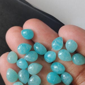 May include: A collection of small, polished, teardrop-shaped gemstones in a vibrant turquoise-blue color. These smooth, opaque stones feature subtle white veining and a glossy finish, presented as a group of individual loose cabochons.