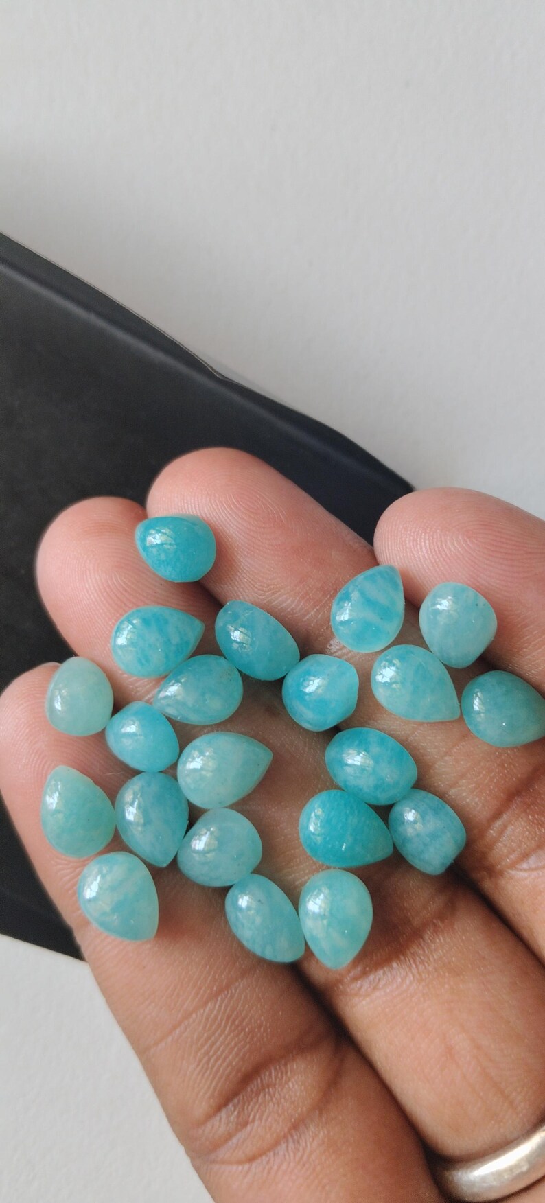 May include: A collection of small, polished, teardrop-shaped gemstones in a vibrant turquoise-blue color. These smooth, opaque stones feature subtle white veining and a glossy finish, presented as a group of individual loose cabochons.