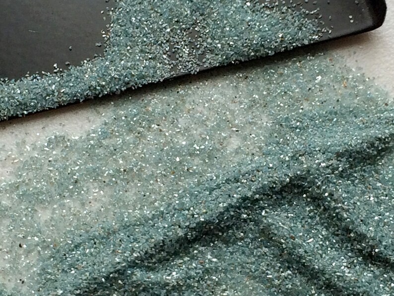 May include: A close-up of a pile of small, light blue glass pieces. The glass pieces are scattered on a white surface.