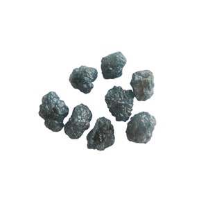 May include: A group of nine dark gray, rough, and unpolished diamonds. The diamonds are scattered on a white background.