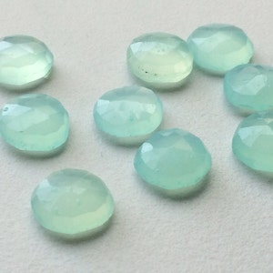 May include: A collection of ten round, faceted gemstones in shades of pale blue-green. The gemstones have a polished, translucent appearance and are arranged on a light-colored surface. Each stone is approximately 0.5 inches in diameter.