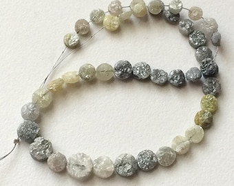 Könnte beinhalten: Eine Strähne runder, facettierter, roher, natürlicher Diamanten in verschiedenen Grüntönen, Grautönen und Weiß. Die Diamanten sind auf einem dünnen Draht aufgefädelt.