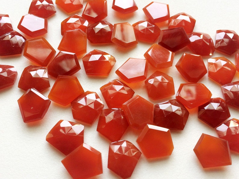 Puede incluir: Una colecci&oacute;n de 30 piedras de cornalina facetadas, cada una con una forma irregular &uacute;nica. Las piedras son de color rojo anaranjado intenso y tienen un acabado brillante.