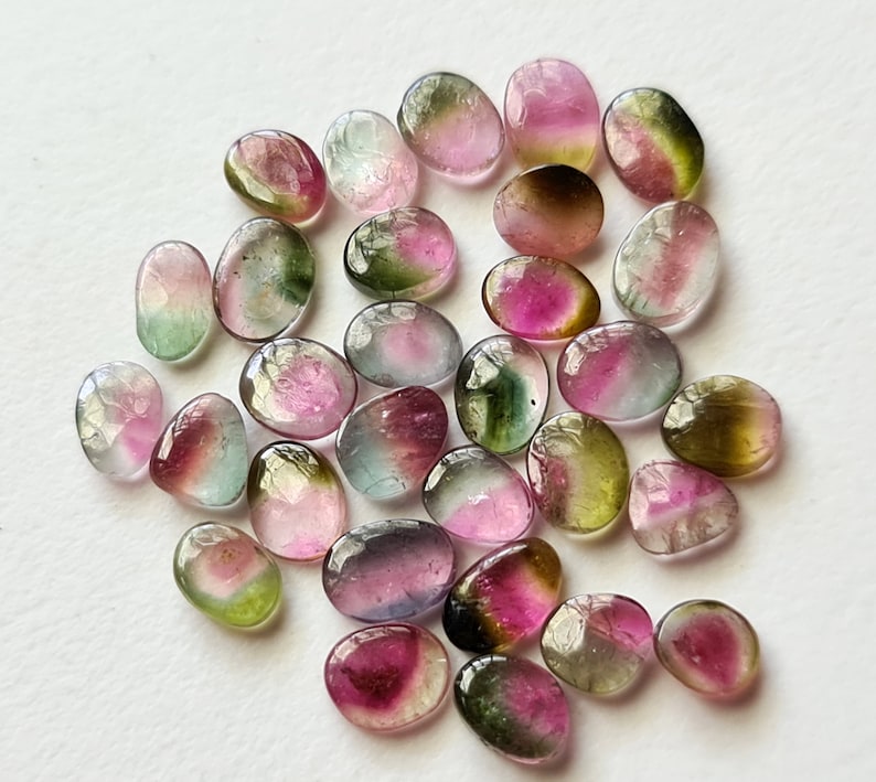 Peut inclure: Une collection de plus de 20 pierres pr&eacute;cieuses lisses de forme ovale, avec un m&eacute;lange de couleurs rose, verte et noire. Les pierres sont roul&eacute;es et polies, cr&eacute;ant une surface lisse et brillante.
