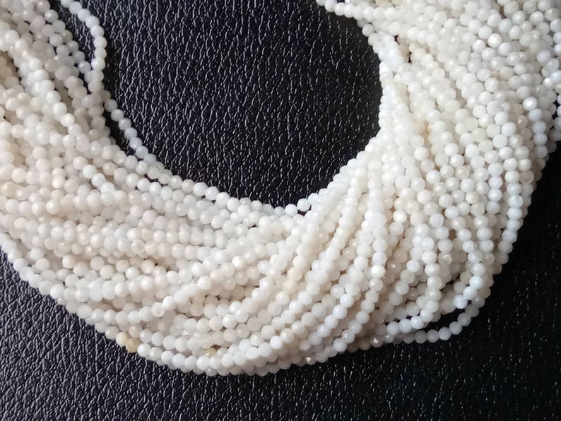 May include: A strand of white moonstone beads, each bead is faceted and has a slightly iridescent sheen.