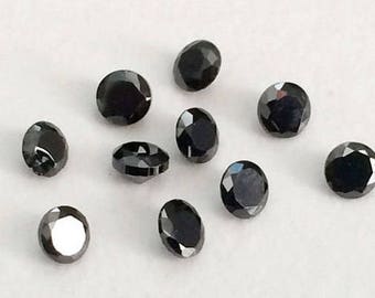 May include: Ten black round gemstones with a faceted cut. The gemstones are scattered on a white surface.