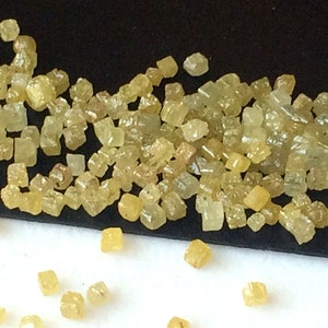 May include: A close-up of a pile of small, yellow, faceted diamonds. The diamonds are scattered on a black surface and some have fallen onto a white surface.
