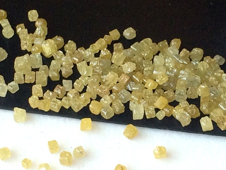 May include: A close-up of a pile of small, yellow, faceted diamonds. The diamonds are scattered on a black surface and some have fallen onto a white surface.