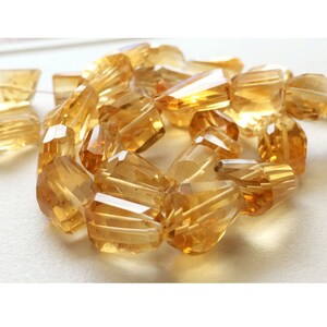 May include: A strand of faceted, golden citrine beads. The beads are cut in a variety of shapes, including rectangular, square, and teardrop. The beads are strung on a clear thread.