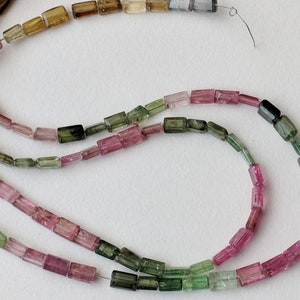 May include: A strand of multi-colored tourmaline beads. The beads are faceted and have a rectangular shape. The colors of the beads are pink, green, and brown.