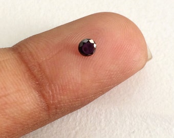 May include: A small, round, dark purple gemstone on a finger.