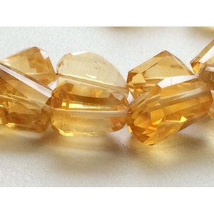 May include: A close-up of a strand of faceted, golden citrine beads. The beads are cut into a variety of shapes, including round, oval, and square. The beads are strung on a clear thread.